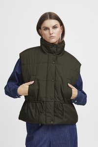 Knee-pikkune, oliivrohelise värvi paks vest kõrge kraega. Omab nööpklappe, küljetaskuid ja tõmbluku sees oleva vöökohtade reguleerimist. Kantud teksasärgi üle.