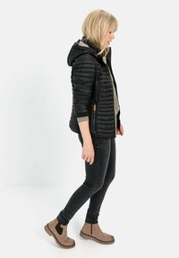 Sort pufferjakke med hætte, sidelommer, båret over en grå top, parret med mørke skinny jeans og beige ankelsko.