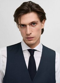 Gilet bleu marine foncé sur une chemise blanche, accompagné d'une cravate noire. Tissu lisse avec une coupe ajustée. Le modèle a des cheveux mi-longs et une expression neutre.