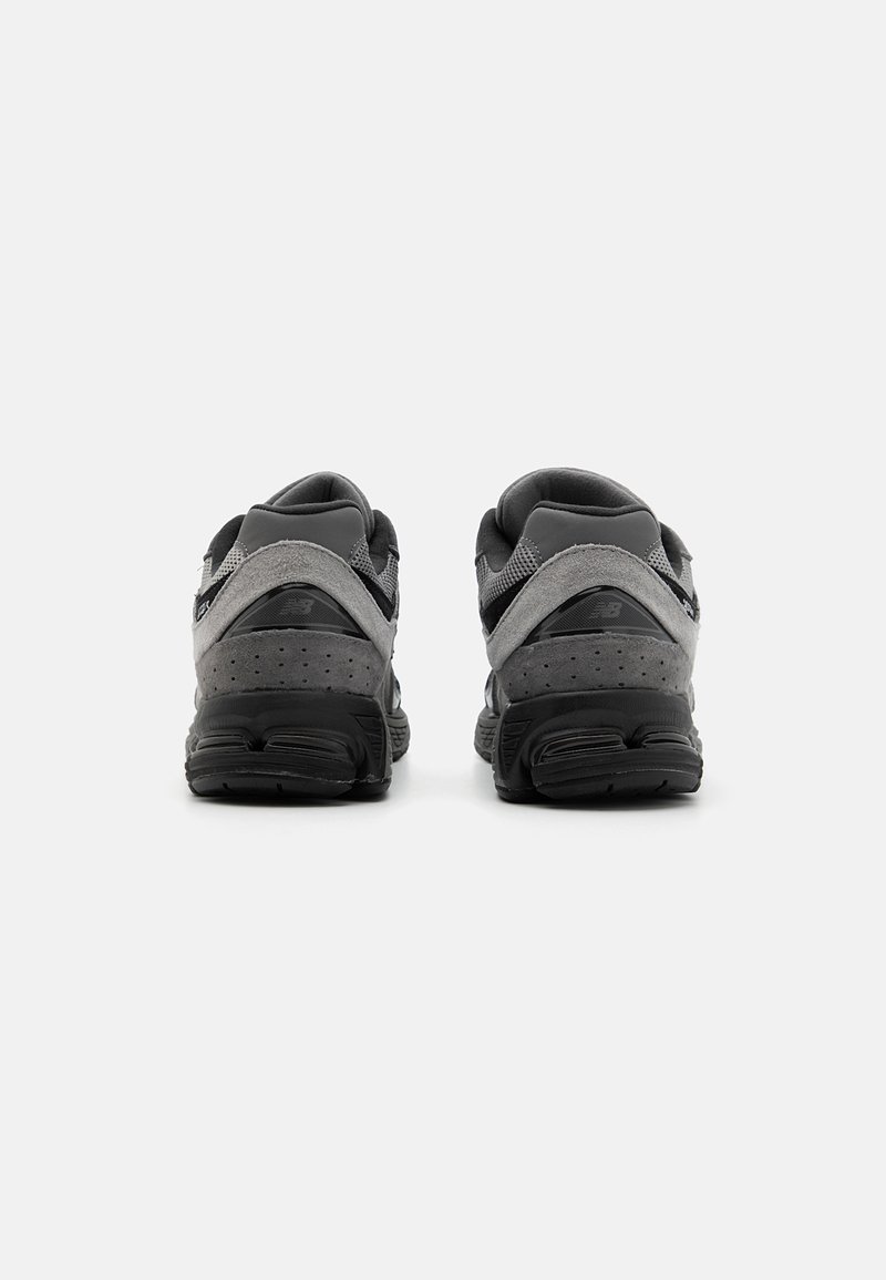 Une paire de chaussures de sport noires et grises vue de l'arrière, avec des semelles rembourrées et des détails en daim perforé sur un fond blanc.