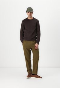 Brauner Sweatshirt, olivgrüne Hose, olivfarbene Mütze und braune Sneaker. Einfaches Design mit normalem Schnitt und weicher Textur.