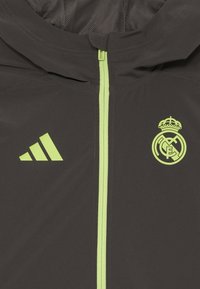 Mörkgrå jacka med framdragkedja och huva. Har en ljusgrön dragkedja och detaljer, samt inkluderar Real Madrid-logotypen och Adidas-stripes.