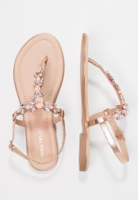 Pari of rose gold tas sandalit me zbukurime me gurë në shina dhe buckles rreth këmbës, një këpucë e treguar nga lart dhe një nga ana.