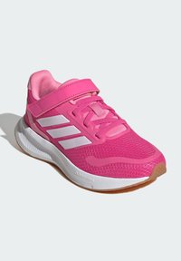 Baskets de sport roses avec dessus en mesh, rayures blanches, col rembourré, sangle velcro ajustable et semelle en caoutchouc avec un motif texturé.
