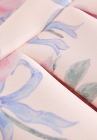 Detail měkké tkaniny se světle růžovým pozadím a jemnými modrými a zelenými květinovými akvarelovými vzory.