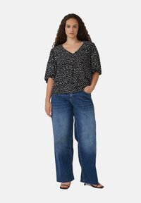 Blouse noire avec des taches blanches, décolletée en V, manches courtes bouffantes. Associée à un jean bleu à jambes larges. Texture de tissu lisse, coupe décontractée.