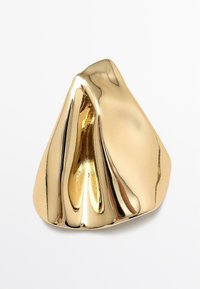 Bague abstraite ton or avec une surface lisse et réfléchissante, présentant des courbes ondulantes et une finition polie, formant une structure sculpturale.