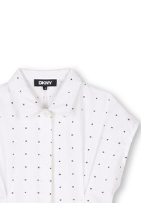 Camicia bianca con colletto a punta e maniche corte, decorata con un motivo di piccole lettere nere e cuori, marchiata DKNY.