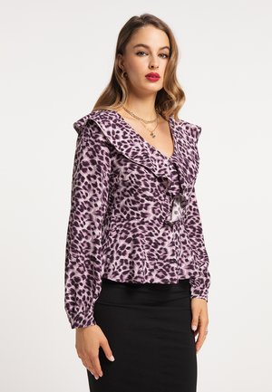 Lila Leopardenmuster-Bluse mit Rüschenausschnitt und langen Ärmeln, aus glattem Stoff. Das Modell kombinierte sie mit einem schwarzen, figurbetonten Rock.