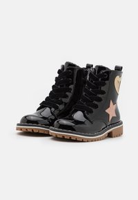 Botines de cuero negro brillante con diseño de cordones, con detalles de estrella y corazón en oro rosa, y una suela resistente de goma marrón.