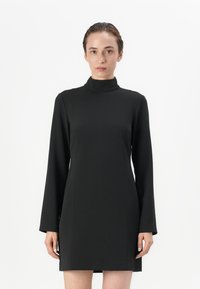 Robe noire à col montant en tissu lisse, dotée de manches longues et d'une coupe évasée, avec une longueur au-dessus du genou et un design minimaliste.