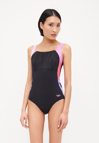 Maillot de bain noir avec des accents roses et violets, présentant un col carré, des bretelles larges et un tissu lisse et extensible. Logo visible.