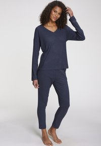 Navy blue ribbed loungewear set featuring a long-sleeve V-neck top and fitted pants with ankle-length cuffs. Soft texture, casual design.