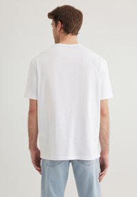 White cotton t-shirt with short sleeves, round neckline, relaxed fit, and no visible patterns or designs, paired with light blue denim jeans.