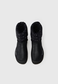 Botines negros hasta el tobillo con un acabado suave y brillante y un puño de lana texturizado. El puño presenta un sutil patrón tejido y costuras en contraste.