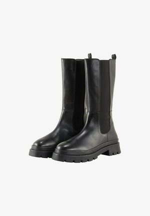 Bottines noires avec une finition en cuir lisse, des panneaux latéraux élastiques et des semelles en caoutchouc épaisses. Dotées de languettes pour un enfilage facile.