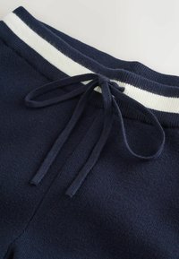 Navy blue knitted sweatpants with white stripes on the elastic waistband, featuring a drawstring for adjustable fit and smooth texture.