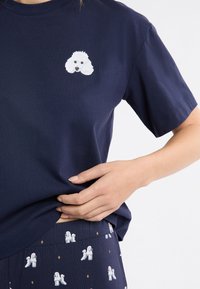 Granatowy bawełniany t-shirt z haftowaną białą twarzą pudla na piersi; noszony z wzorzystymi spodniami z motywem pudli.