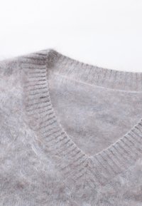 Maglione lavorato a maglia grigio chiaro con scollo a V, collo a costine e una texture morbida e fluffy con sottili variazioni di colore.