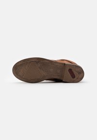 Suela de zapato de goma marrón con patrones texturizados, diseños geométricos y un logotipo rojo de la marca, con un aspecto limpio y desgastado.
