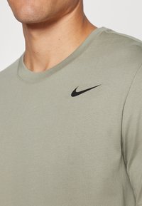 Oliivroheline puuvillane T-särk ümmarguse kaelusega ja lühikeste varrukatega. Vasakul rinnal on must Nike'i logo. Lihtne, keha lähedal istuv disain.