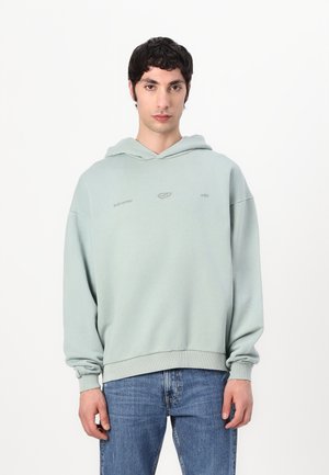 Light green hoodie with a relaxed fit, ribbed cuffs, and hem. Features minimal branding. Paired with blue jeans for casual style.