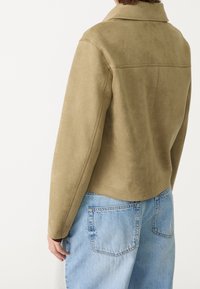 Olivgrön konstläderjacka med spaltdesign, figursydda axlar och långa ärmar. Baksidan har en ren, minimal design.