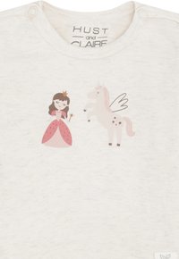 Ragazza in abito rosa che tiene una bacchetta accanto a un unicorno con ali e criniera rosa su una maglietta per neonati di colore grigio chiaro.