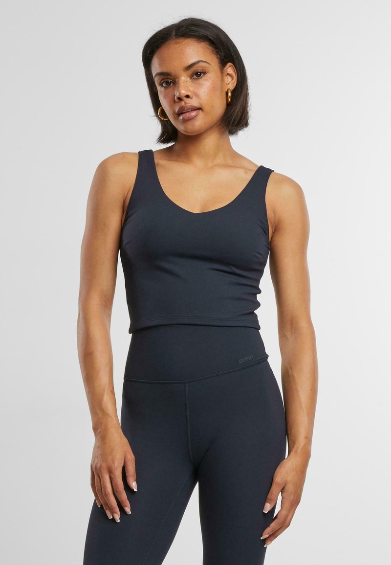 Tmavomodrý športový crop top s výstrihom do V, tenkými ramienkami a priliehavým strihom. Vyrobený z hladkého, elastického materiálu, perfektne sa hodí k legínam s vysokým pásom.