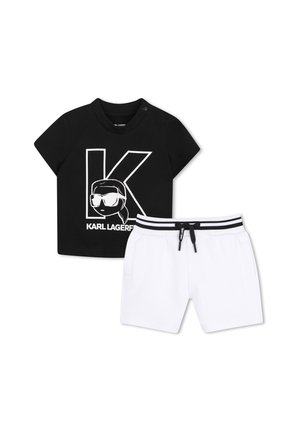 Zwart T-shirt met korte mouwen met een grote "K" en cartoongezicht, gecombineerd met witte short met zwart gestreepte elastische tailleband en trekkoord.