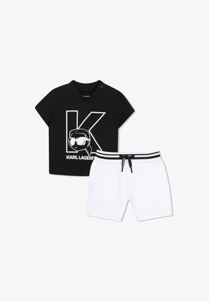 Zwart T-shirt met korte mouwen met een grote "K" en cartoongezicht, gecombineerd met witte short met zwart gestreepte elastische tailleband en trekkoord.