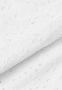 La tela blanca bordada presenta patrones intrincados con motivos de hojas y flores, caracterizados por detalles recortados y una textura suave.