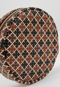 Runde Ledertasche mit strukturierten Oberflächen, die mit sich gegenseitig überlappenden braunen und schwarzen Formen auf einem cremefarbenen Hintergrund gemustert ist. Mit Reißverschluss.