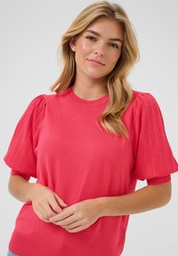 Pull coral avec des manches bouffantes côtelées et un col rond. Matière tricotée douce, corps ajusté et texture subtile sur les manches.