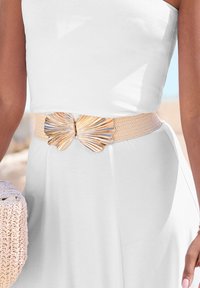 Tkani pojas bež boje s metalnom kopčom u obliku leptira koja ima teksturiranu zlatnu i srebrnu završnu obradu, nosi se preko bijele haljine.