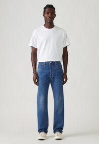 White short-sleeve t-shirt paired with blue denim jeans. Jeans feature a straight-leg cut, classic five-pocket style, and subtle fading.