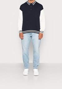Suéter azul marino y blanco con cuello de canalé, botones y detalles a rayas. Combinado con jeans azul claro y zapatillas blancas.