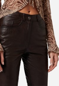 Bruine leren broek heeft een aansluitend ontwerp, voorzakken en een knoopsluiting. De textuur lijkt glad met een subtiele glans.