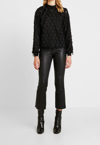 Maglietta nera a maniche lunghe con texture, abbinata a pantaloni in pelle nera a gamba skinny e stivaletti.