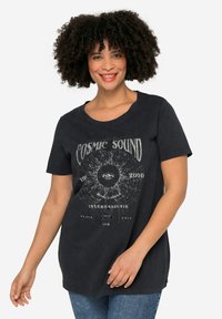 Camiseta de algodón negra con un corte relajado, que presenta un diseño gráfico con el texto "Sonido Cósmico" y un motivo de ojo en blanco, de manga corta.