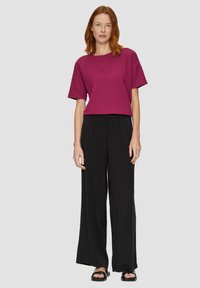 Fuchsia gestructureerde top met korte mouwen gecombineerd met losse zwarte broeken. De outfit heeft een relaxte fit en eenvoudige zwarte sandalen.