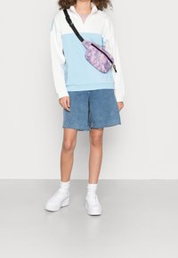 Hellblaues und weißes Zip-up Sweatshirt, Jeansshorts mit ausgefransten Säumen, lila Camouflage Umhängetasche und weiße Plattform Sneaker mit Knöchelsocken.