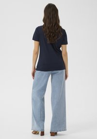 Camiseta de color azul marino con mangas cortas, combinada con unos jeans de pierna ancha de color azul claro, mostrando un ajuste relajado y un diseño simple y clásico.