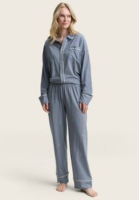 Gestreepte blauwe pyjama-set, bestaande uit een button-up shirt met een zak en broek met elastische tailleband, gemaakt van zachte stof met boorden op de mouwen.