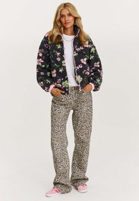 Fleece bunda s ružovým kvetinovým vzorom, vysokým golierom a zipsovým zapínaním, v kombinácii s širokými nohavicami s leopardím vzorom a ružovými teniskami.