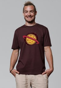 Bordeauxfarbenes Baumwoll-T-Shirt mit einem Grafikdesign eines Pizzastücks, umgeben von einem roten Ring, vor einem strukturierten Hintergrund mit Sternen.