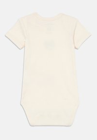 Kortermet body i kremfarge laget av mykt stoff, med rund hals og trykknapper nederst for enkel påkledning.