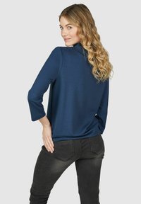 Navyblauw shirt met driekwartmouwen, ronde halslijn en gladde textuur, gecombineerd met donkere skinny jeans. Achteraanzicht weergegeven.