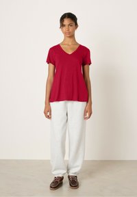 Raudono vyno spalvos V formos kaklo marškinėliai su trumpomis rankovėmis, derinami su šviesiai pilkais sportiniais šortais ir rudais batais su raišteliais; švelni medžiaga, laisvas siluetas.