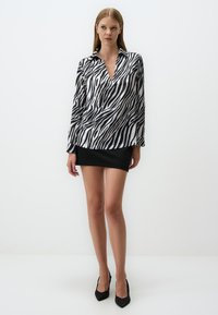 Blusa a stampa zebrà in bianco e nero con scollatura a V, maniche lunghe e texture liscia, abbinata a una mini gonna nera aderente.